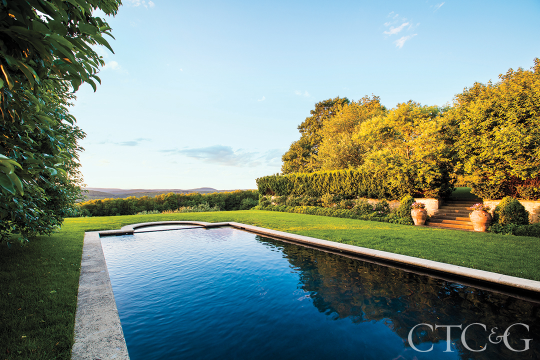 A rectangular pool surrounded by grey stone and a green lawn.