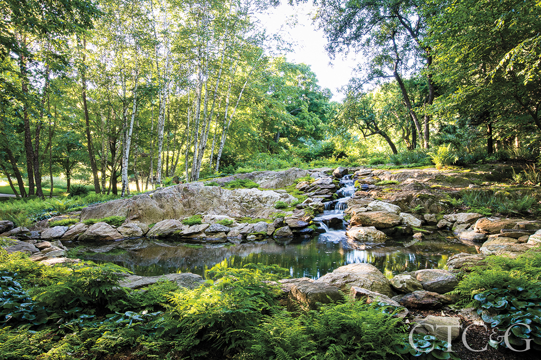 A small waterfall rushes down rocks into a pond.