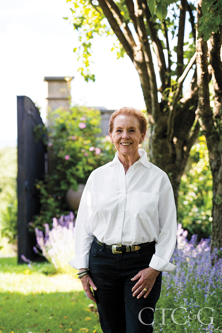 Linda Allard in a white blouse and dark pants standing in her property.
