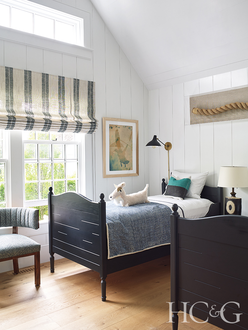 A grey and black twin bed sits in the corner of this child's bedroom, with a window to the left.