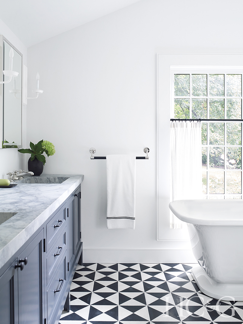 Black and white triangular tiles decorate the floor of an all-white bathroom.