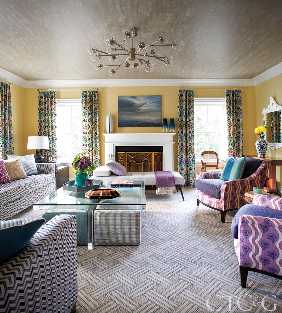 living area with yellow walls, purple patterned chaats and sofas with patterned curtains.