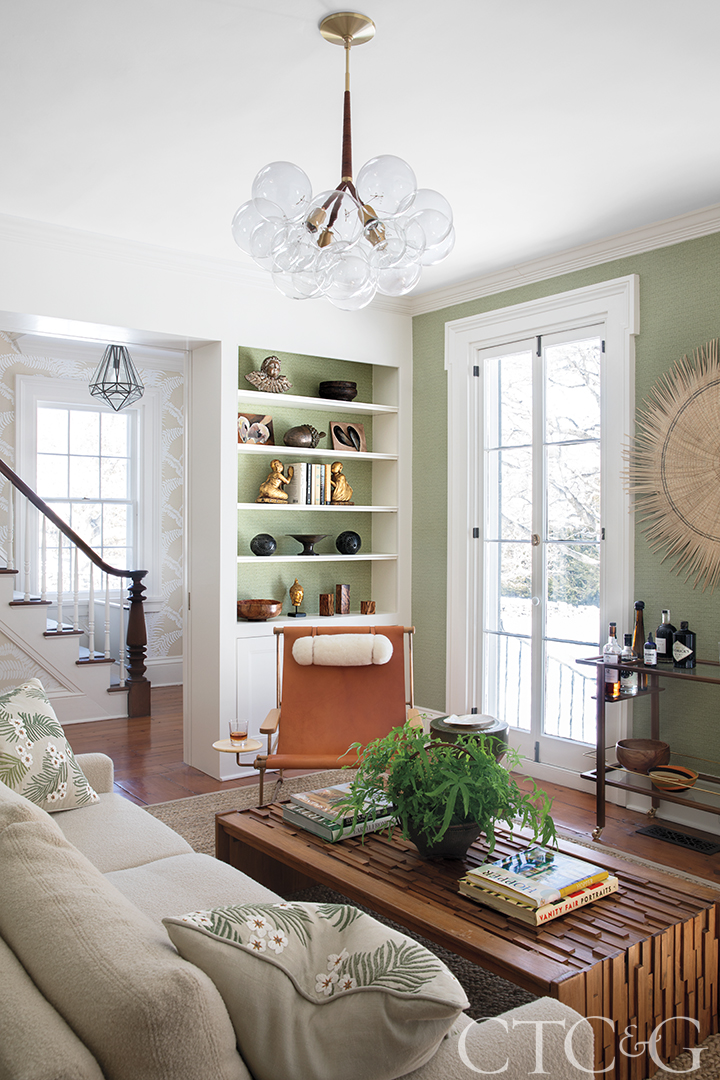 Parlor room with green walls, bookshelf and bar cart.