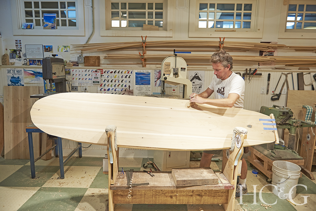 A man working on a wooden surfboard.