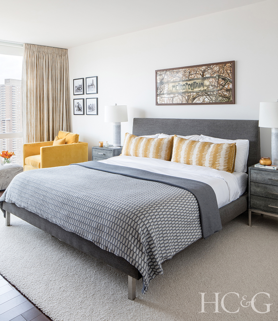A grey full bed with yellow and white striped pillows sits against a white wall.