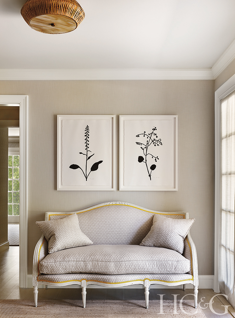 Two prints of plants hang above a light sofa.
