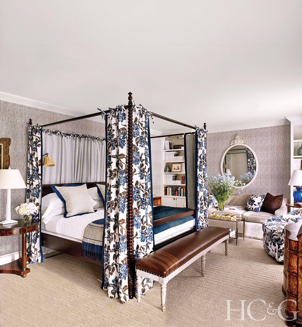 A guest bed canopied with a white, brown, and blue fabric. A brown bench sits at the foot of the bed.