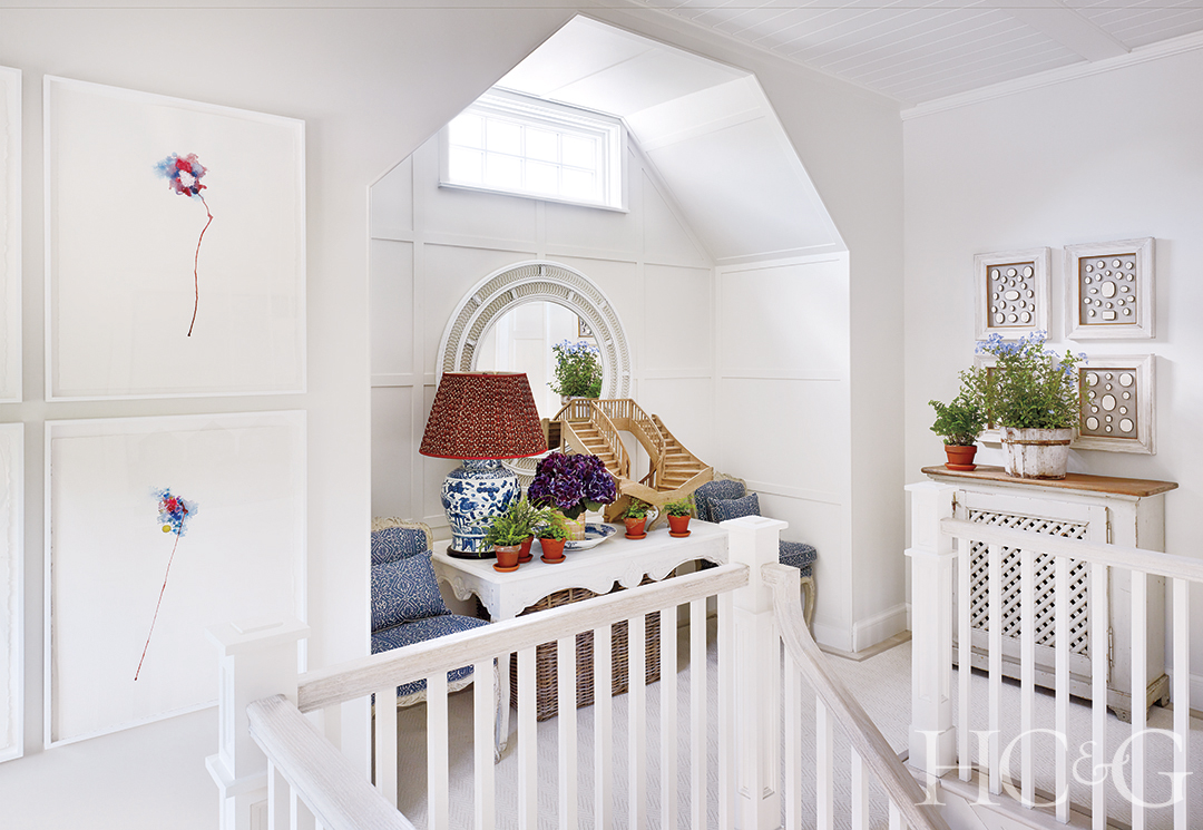 An all-white alcove at the top of the stairs decorated with plants and artwork.