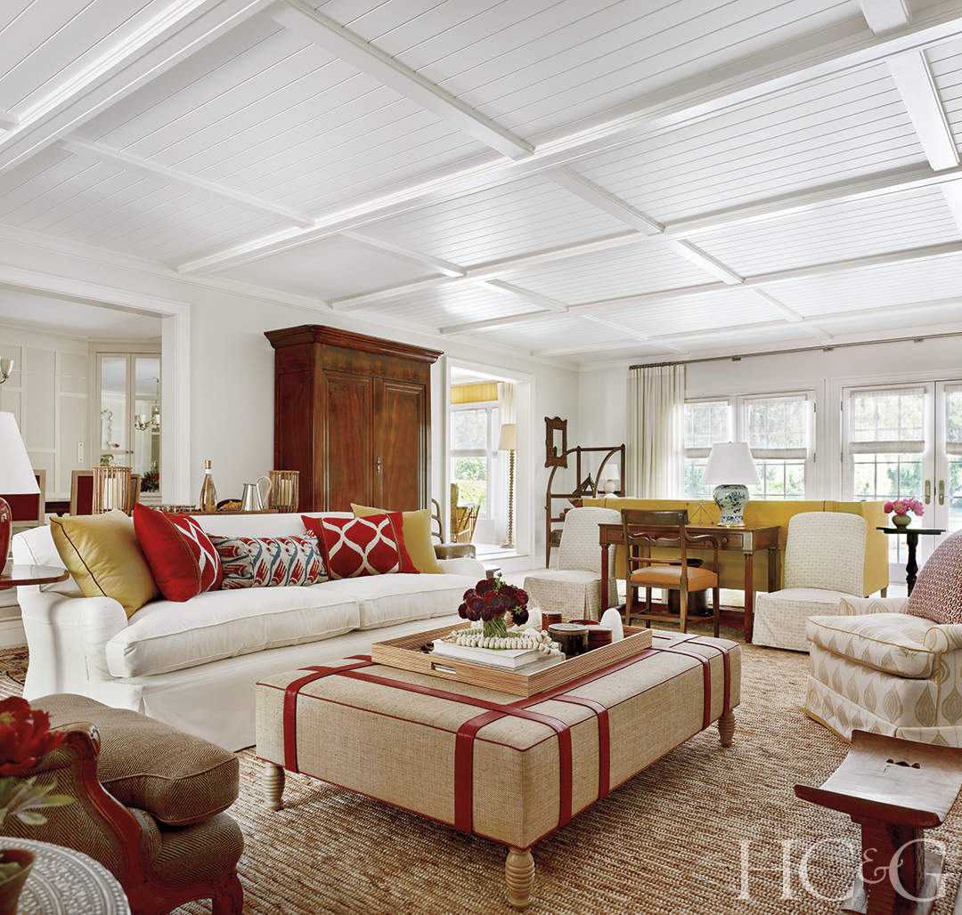A tan table with red detailing is the center of the living room, backed by a white couch.