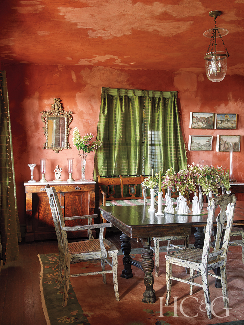 A predominately orange dining room with a green curtain backing the wooden table and white chairs.
