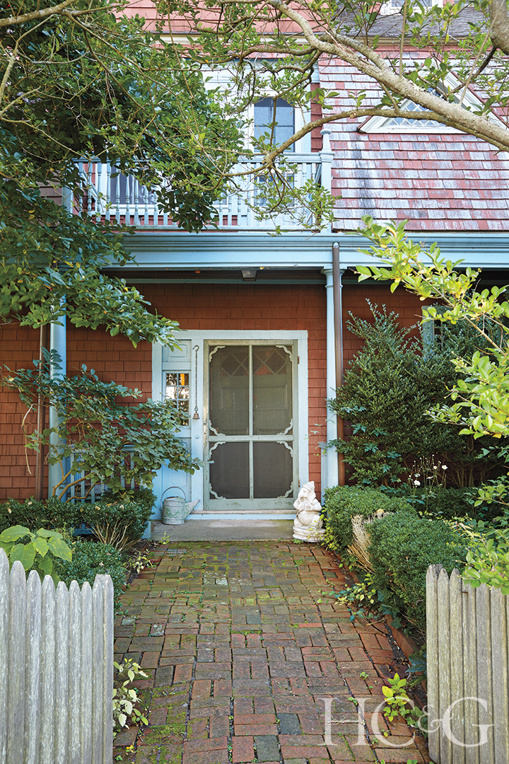 A stone pathway leads to a white door on an orange shingle-style house.