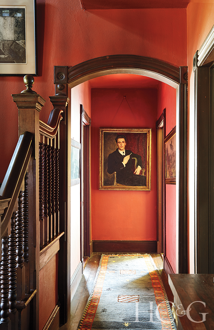 A reddish-orange hallway leading to a framed painting of a man in a suit.