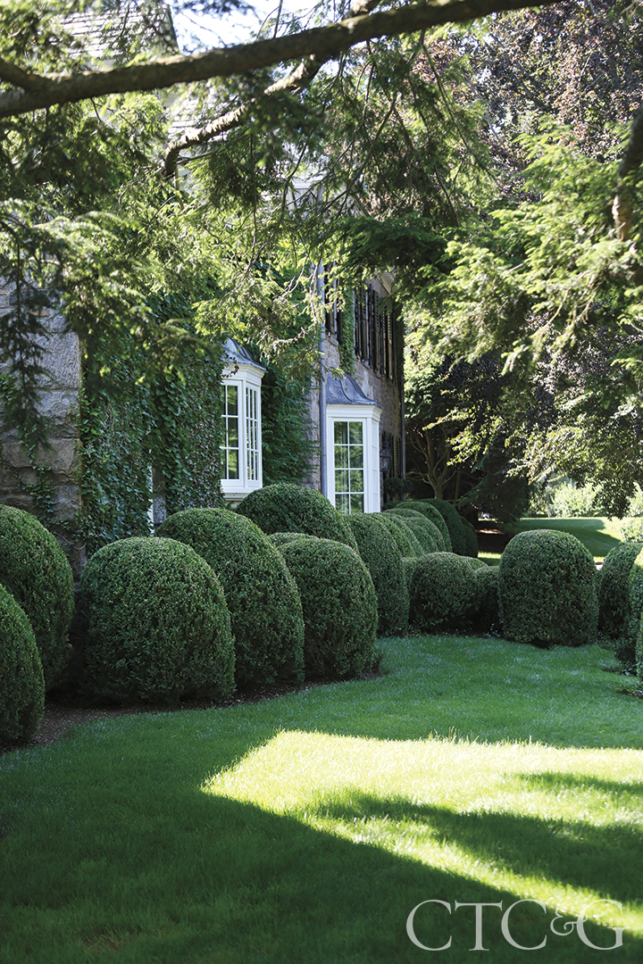 Round boxwood bushes surround the side of a stone house.