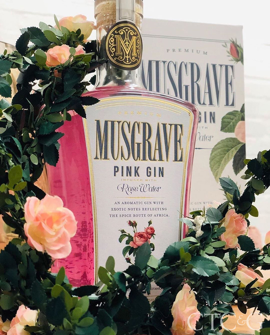 A pink bottle of gin surrounded by pink roses with dark green leaves.