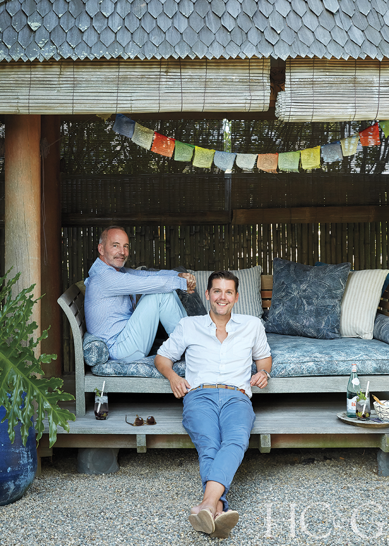Two men wearing blue and white seated at a wooden gazebo, smiling.