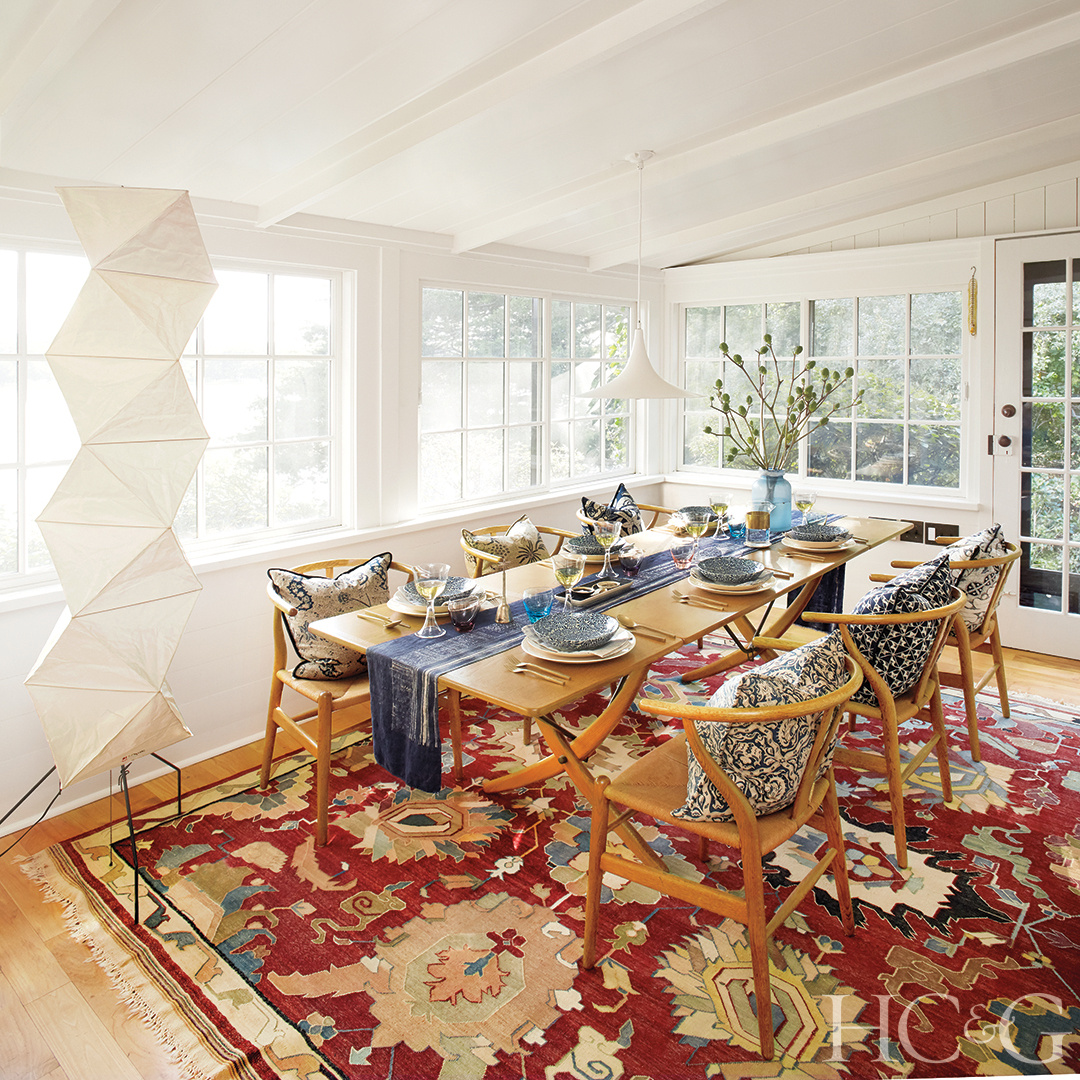 A red carpet brings color to a white dining room with wooden chairs and table.