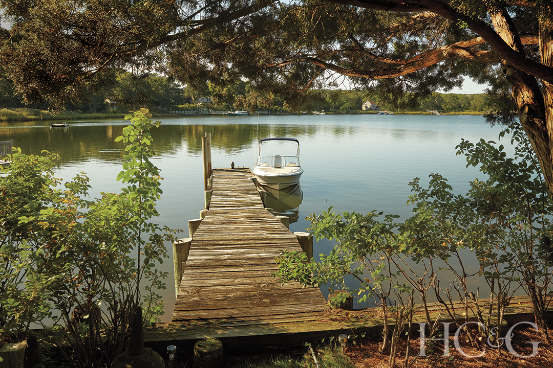 A wooden dock leads out into the water, a white boat is docked on the right side towards the end.