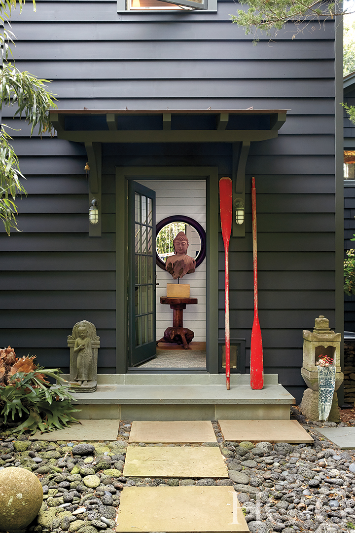 A black house with an open door. Two red oars stand vertically to the right of the door.