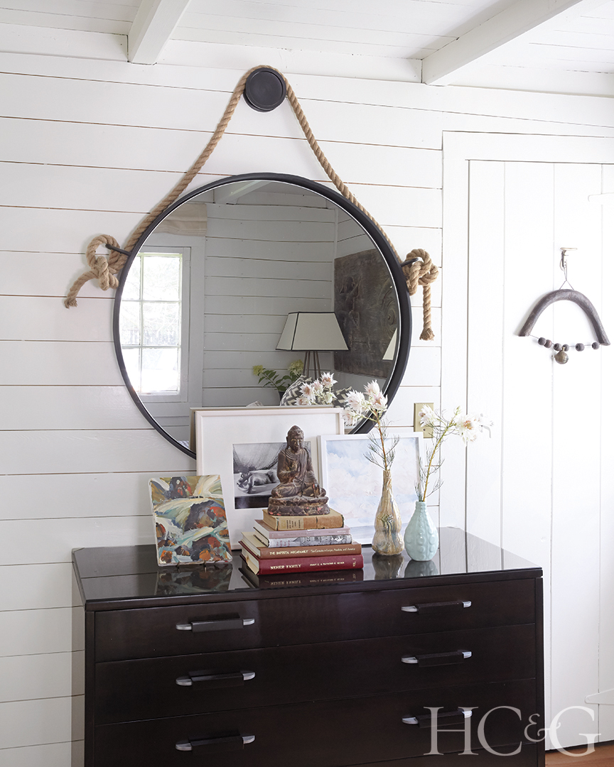 A large round mirror hangs above a dark dresser, in contrast with the white walls.