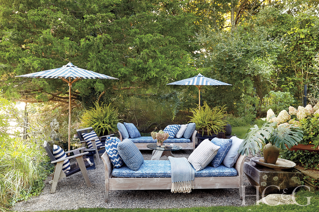 Outdoor chaises cushioned in blue are accompanied by blue lounge chairs and umbrellas in contrast to the green foliage.