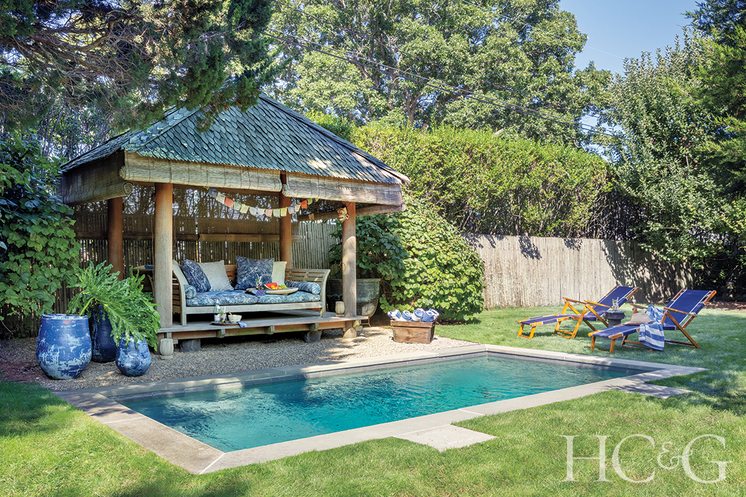 An iron and wood gazebo sits behind a rectangular swimming pool.