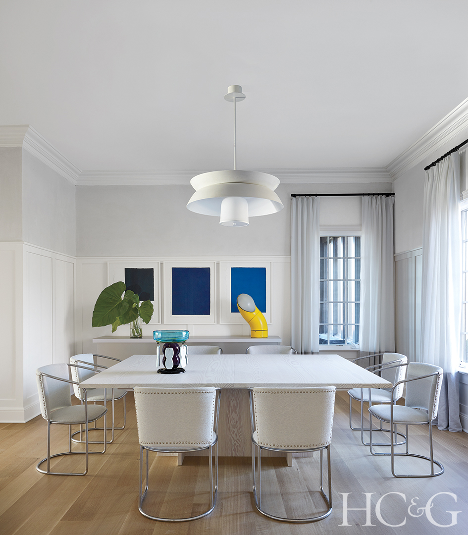 A white square table surrounded by two white chairs on each side. Bright blue canvases hang in the back.