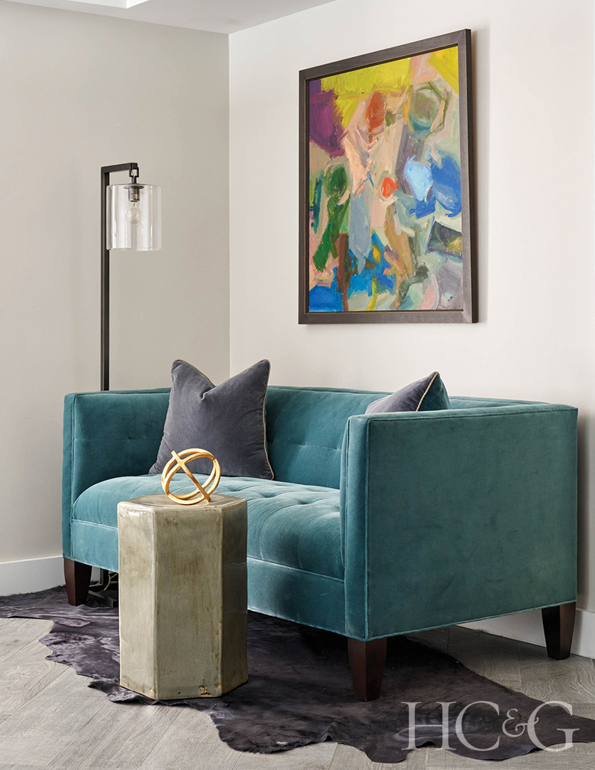 A teal blue couch with an abstract painting on the wall.