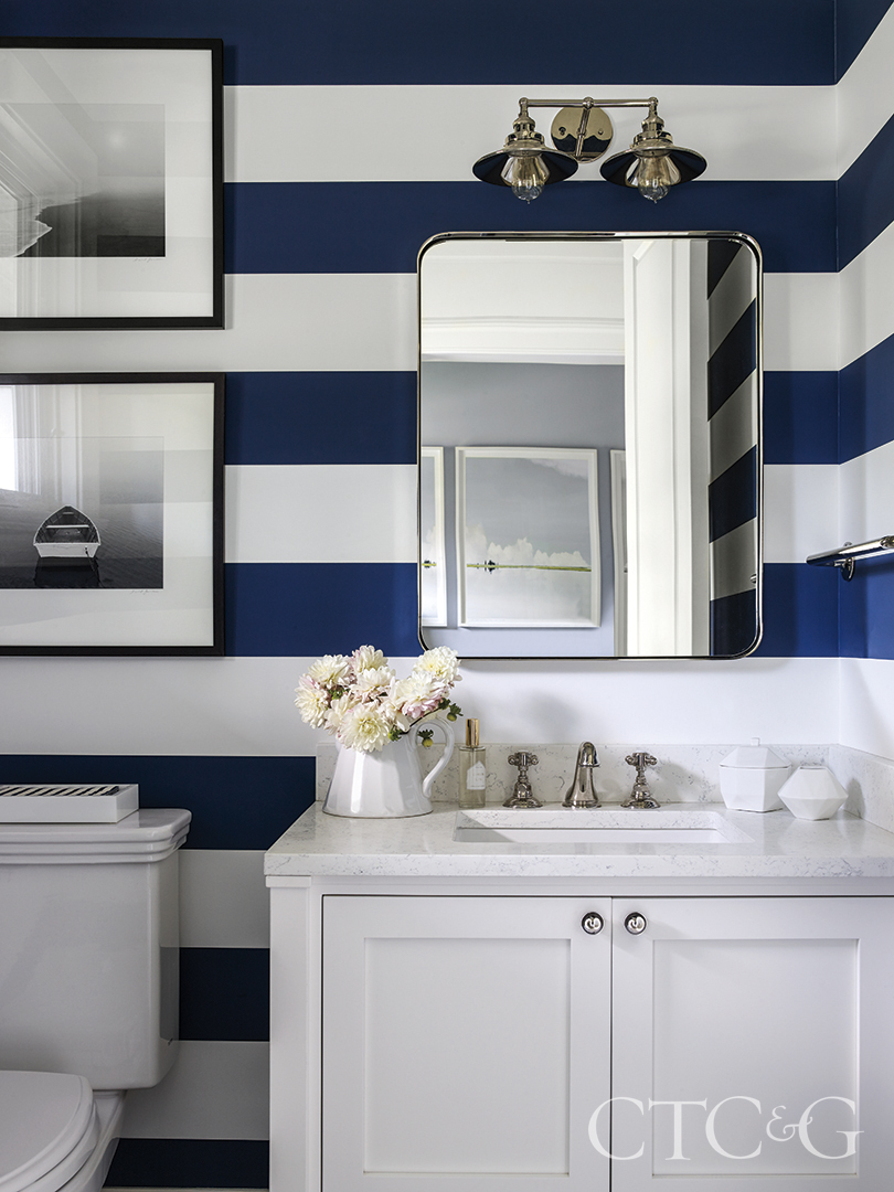bold blue and white stripe wallpaper cover the walls of otherwise white clean lined powder room