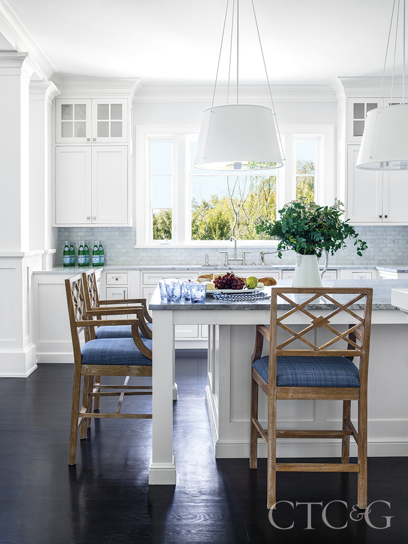 natural light highlights the white marble kitchen and complimentary blue cushioned oak island chairs