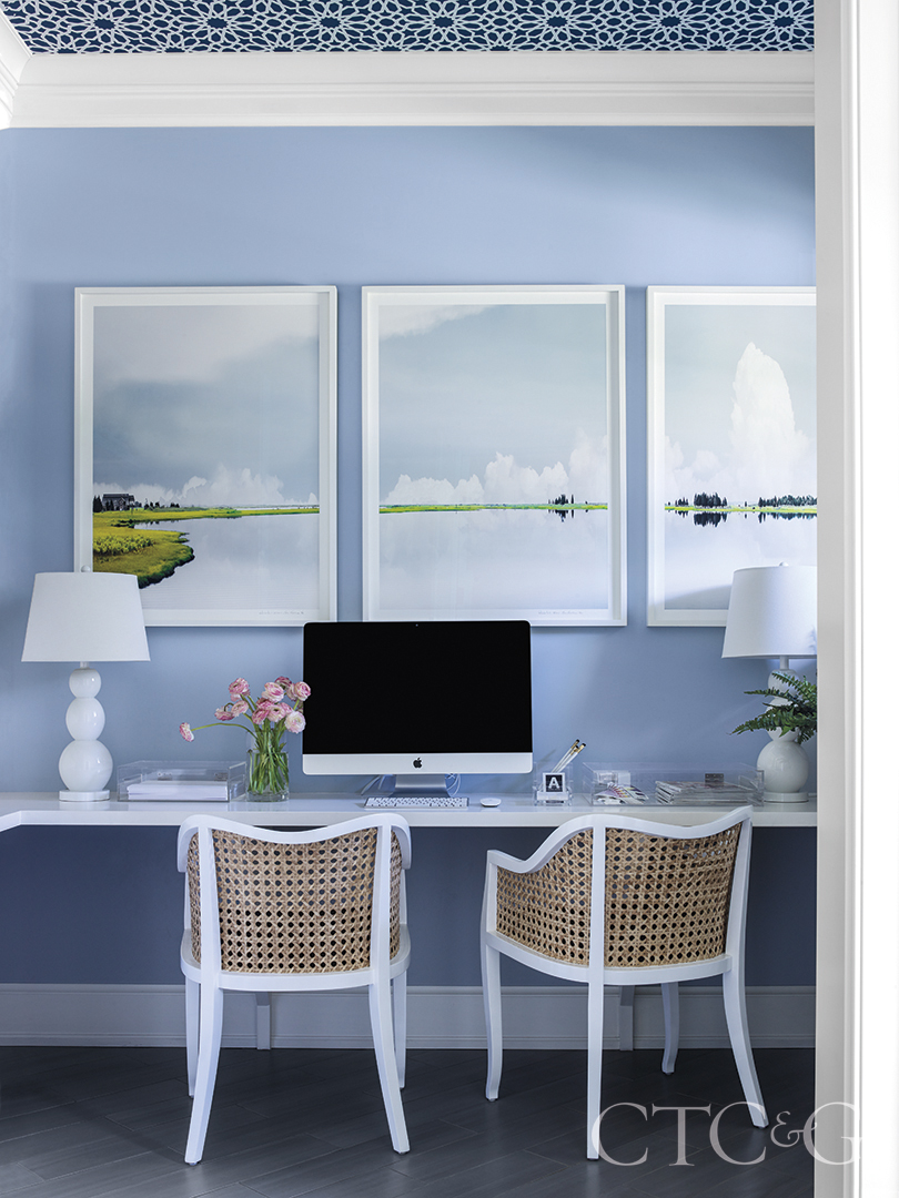 three landscape paintings hang on blue wall atop floating desk in office