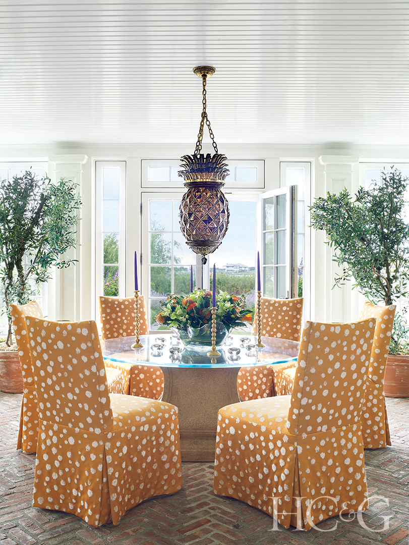brick-paved dining room; orange slipper chairs and pineapple light fixture