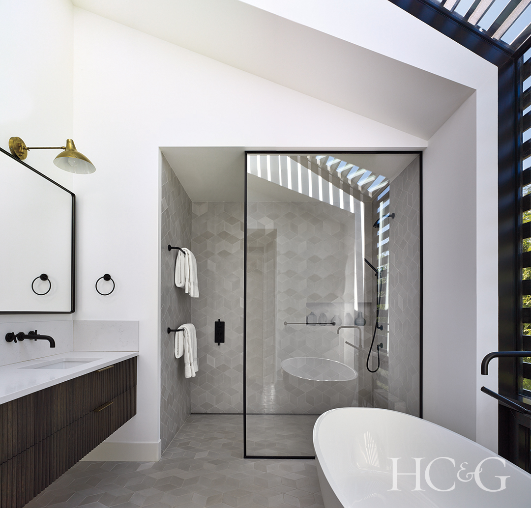 modern white bathroom with black accents; freestanding sink, glass shower, gray tile