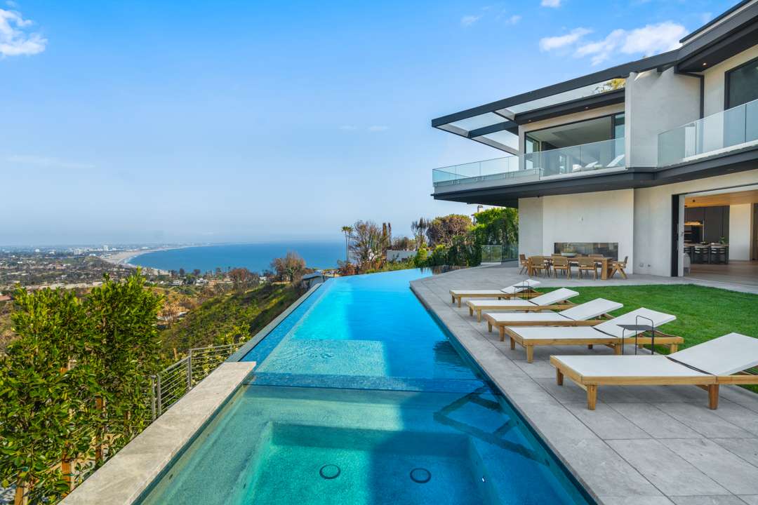 Infinity pool and hot tub surrounded by chaise lounge chairs overlooking Pacific Palisades and ocean
