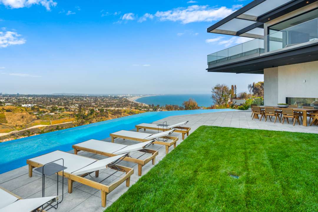 Chaise lounge chairs by infinity pool overlooking Pacific Palisades