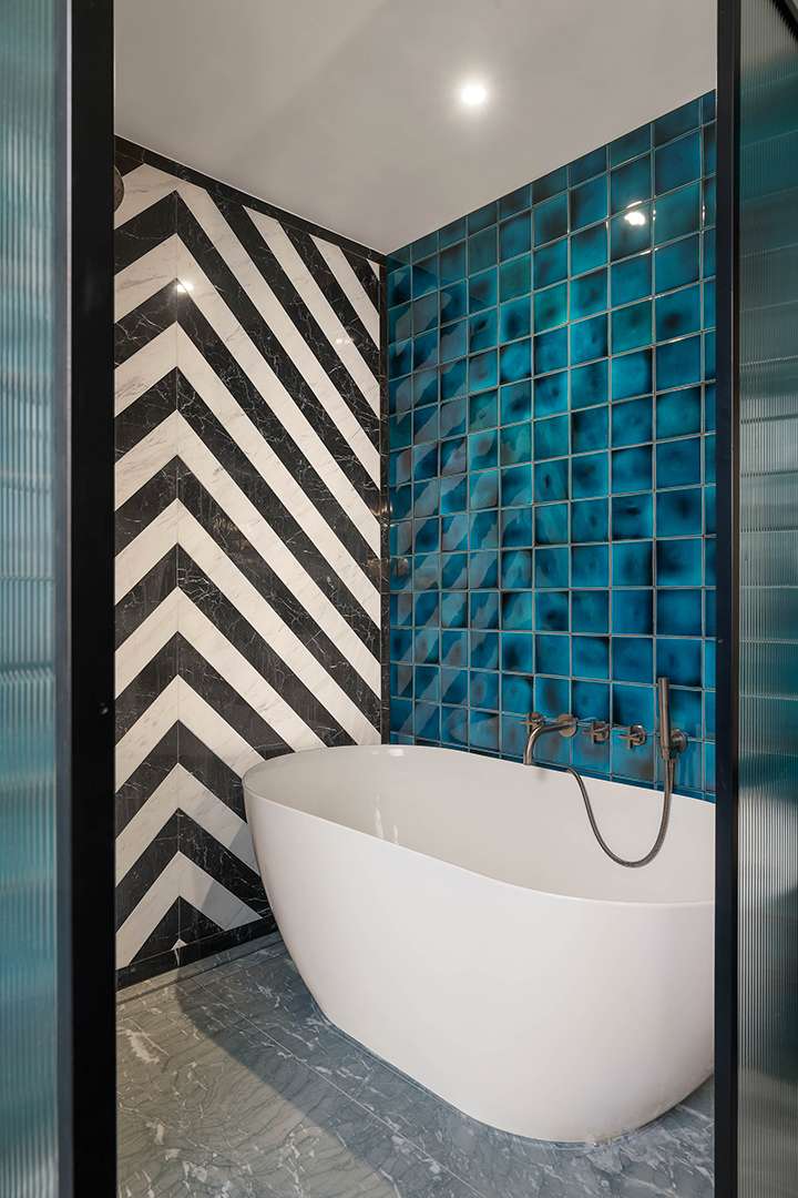 Bathroom with white stand alone tub and blue tile and black and white striped marble on opposite walls