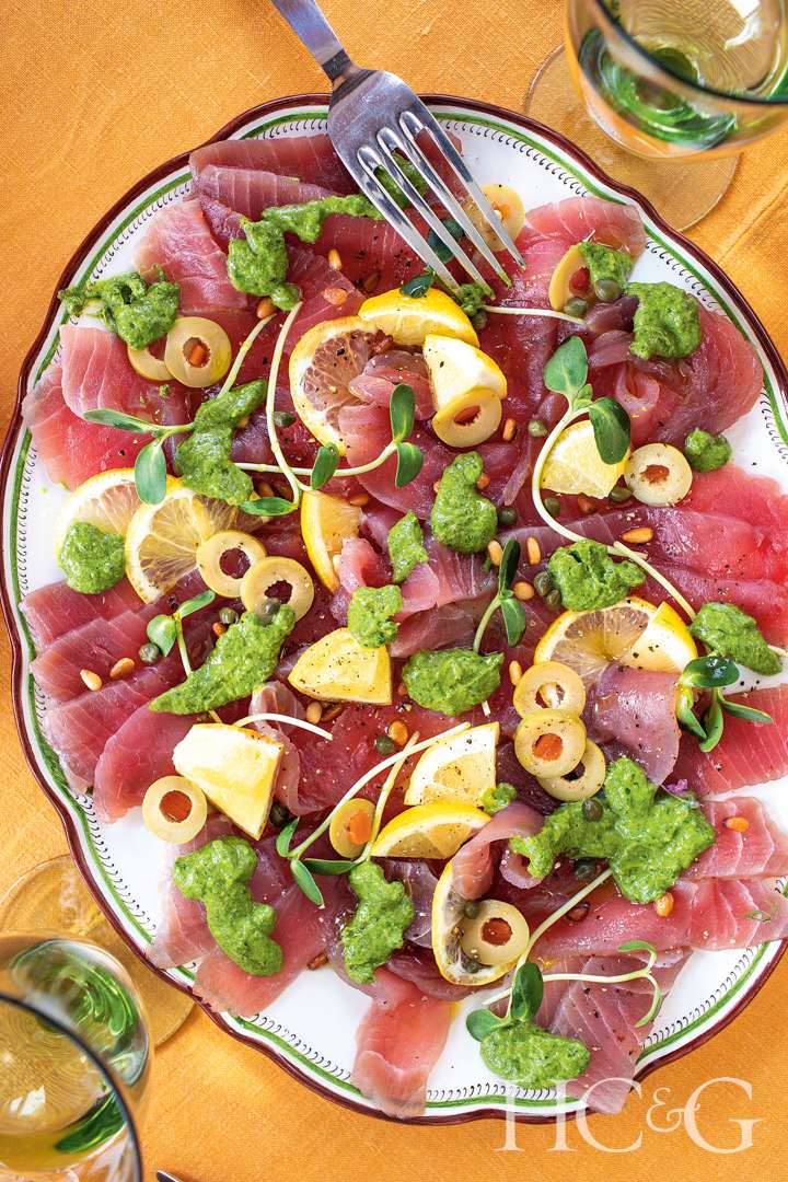 Dish of tuna crudo, with green sauce, olives, pine nuts, and citrus.